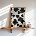 Framed heart cow print wall art on a small rustic shelf, sunlit, creamy white background