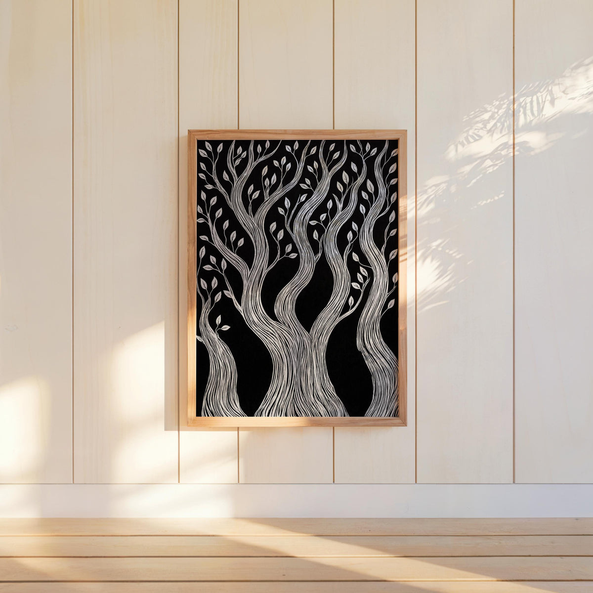 Tall framed black and white forest wall art centered on pale wall, sunlight stripe highlights linocut tree print