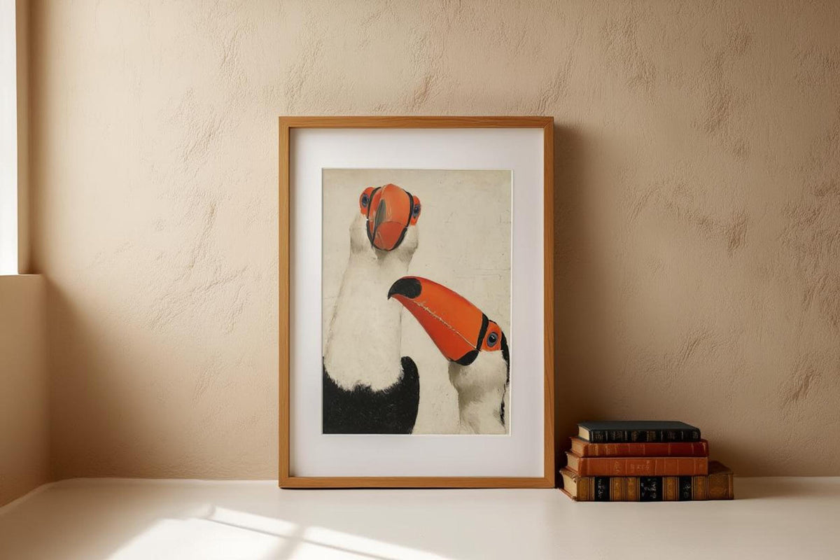 Thin white-framed toucan wall art print centered on floor against plaster wall, small stack of books nearby