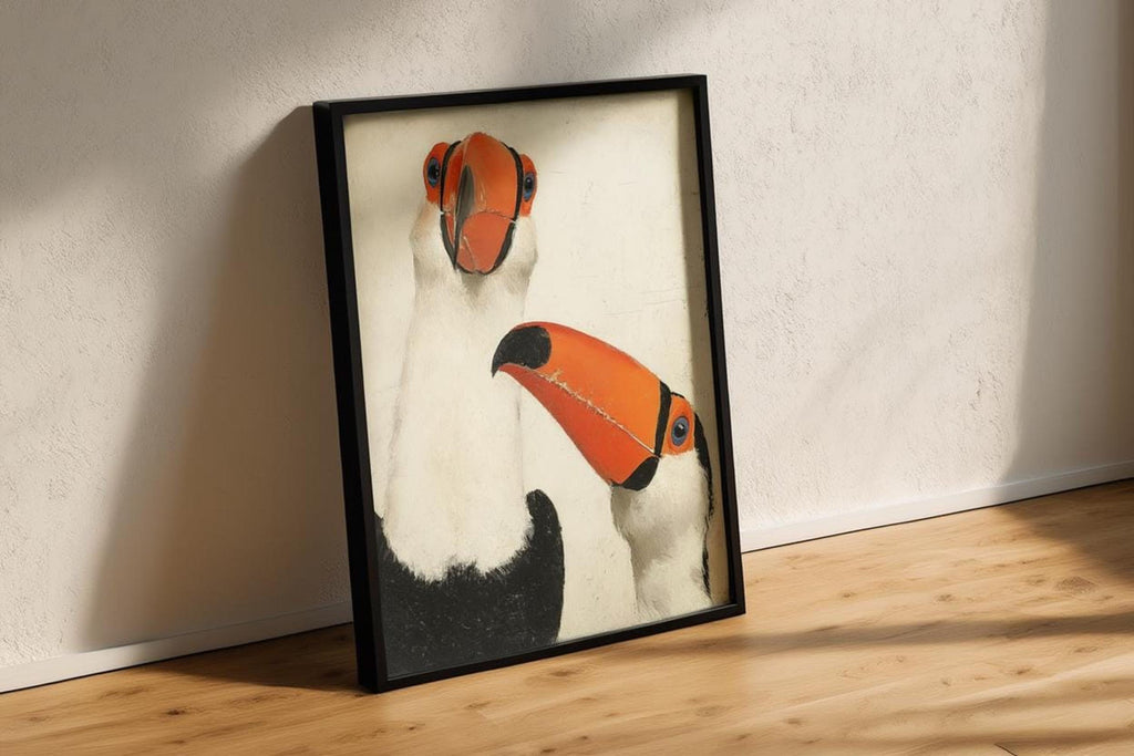 Black-framed toucan wall art print propped against wall, dramatic side shadow, bold orange beaks pop