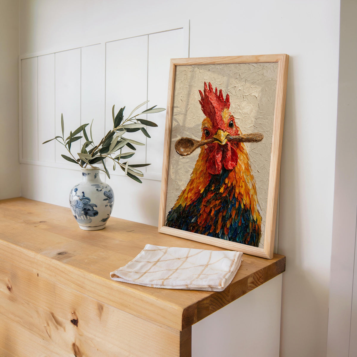 Rooster kitchen wall art resting on a wooden counter with blue vase and linens, chicken kitchen wall art look