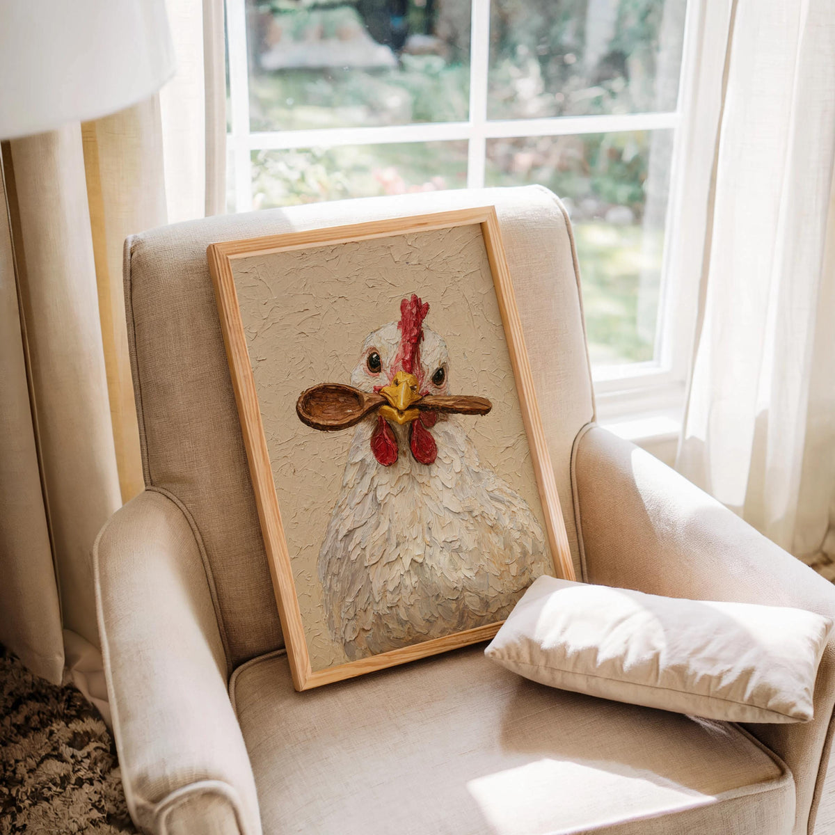 Cozy armchair holding a framed hen holding spoon print by a bright window, cottagecore chicken kitchen wall art