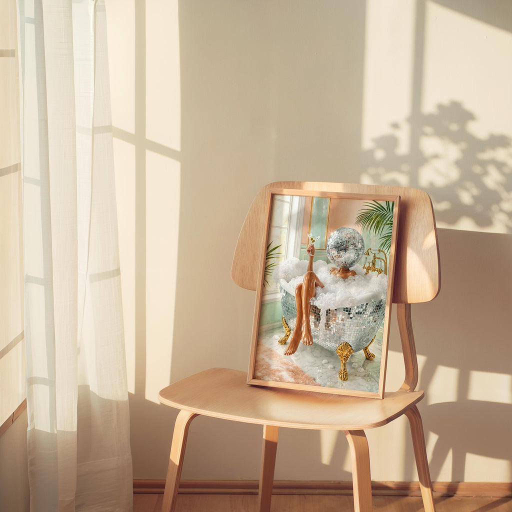 Feminine disco ball bathroom art print resting on a wooden chair, soft window shadows and leafy accents