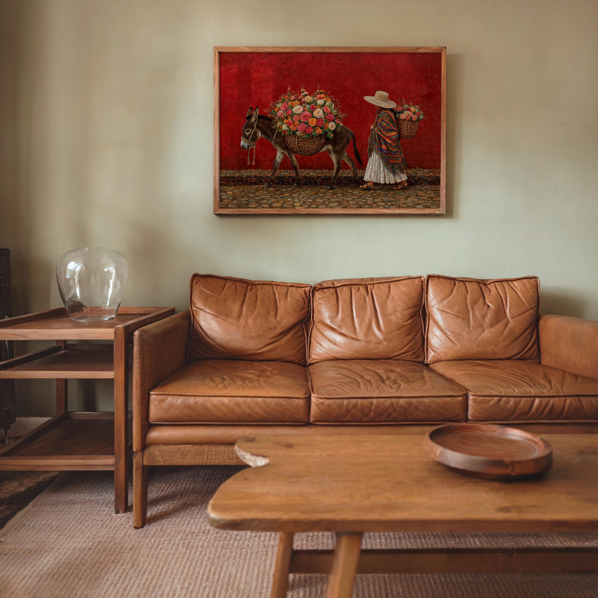 Mexican painting poster above couch, vivid red background, rustic market scene with donkey and floral load, vintage vibe