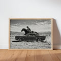 Framed Cowboy and Classic Car Wall Art leaning on hardwood floor, cinematic black-and-white Western print