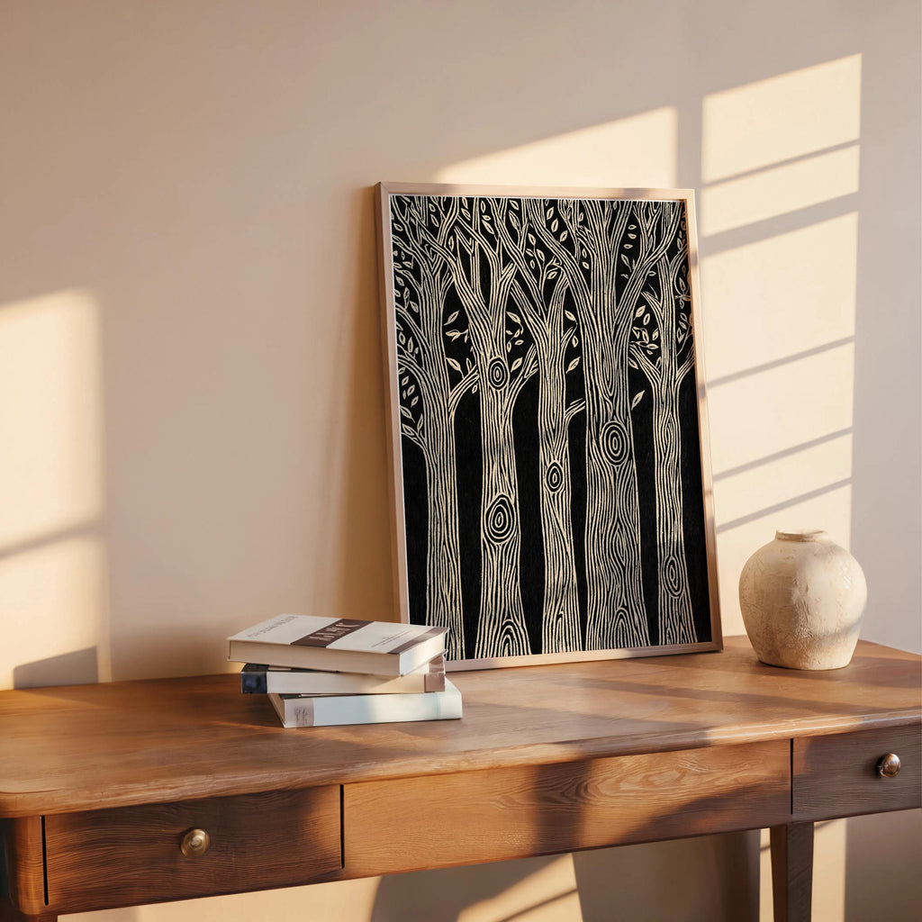 Vertical black and white forest wall art propped on a rustic wooden table with books and pottery, woodcut tree print vibe