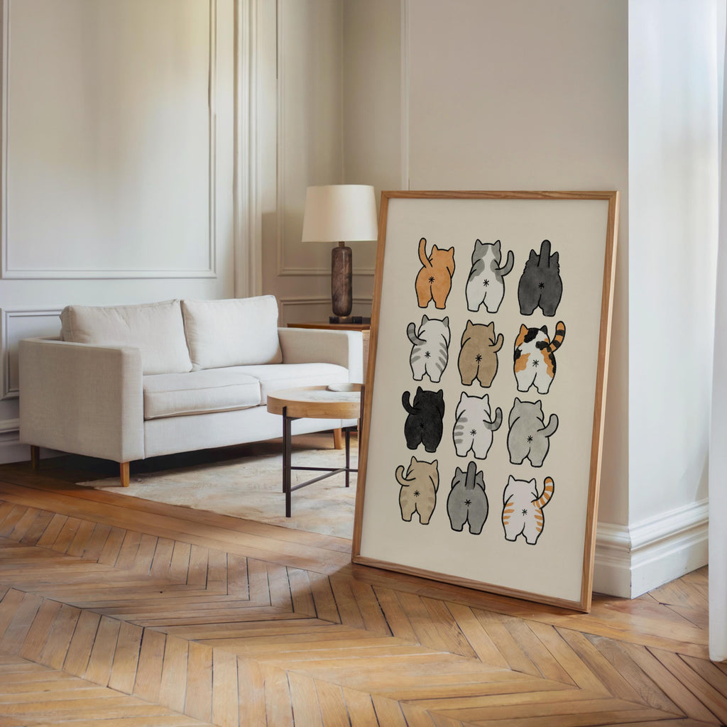 Print propped in a bright living room corner by a couch, 3x4 grid of cartoon cat butts, great cat lover bathroom wall art