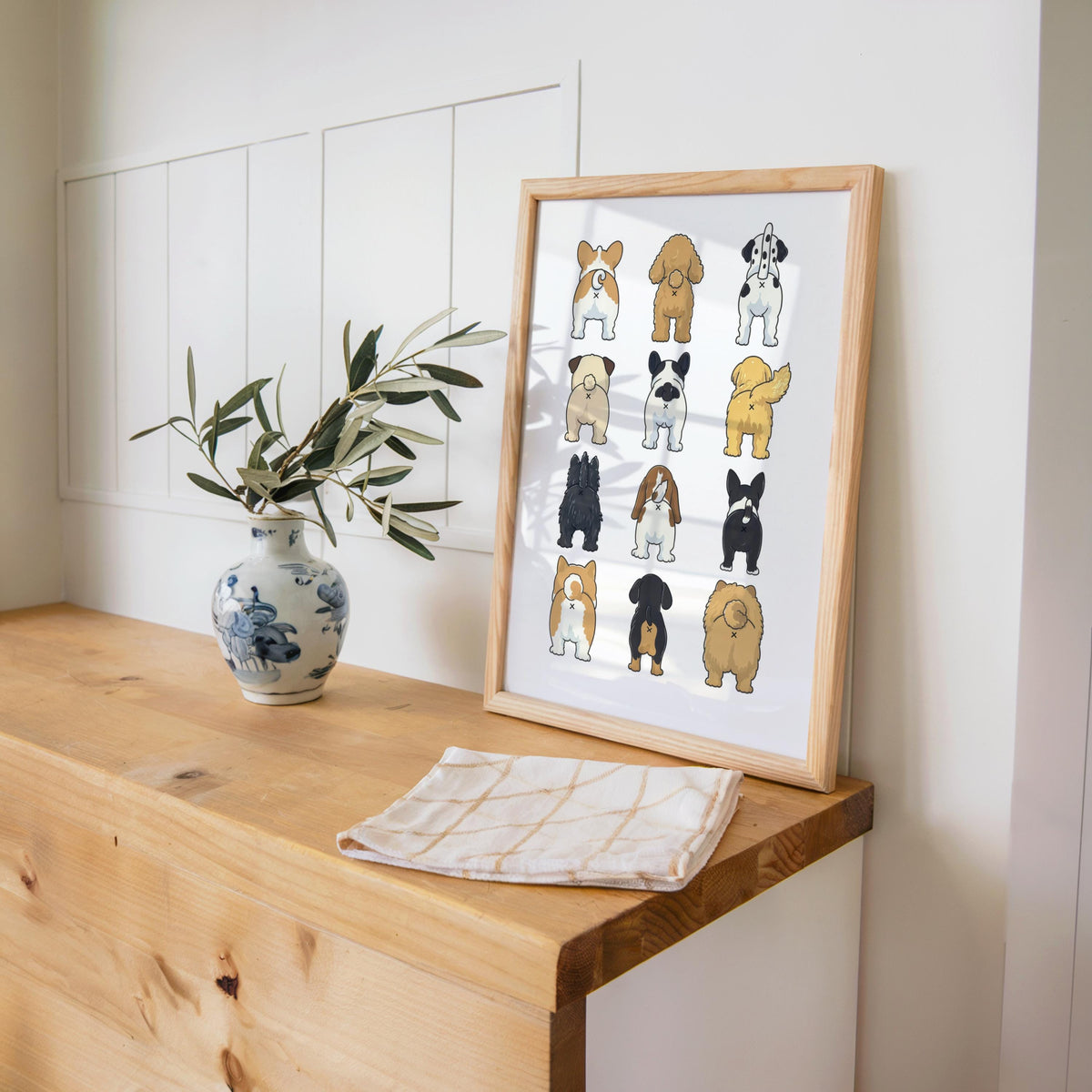 Leaning funny dog butt bathroom art print on an entry bench with plant and towel, quirky toilet wall art