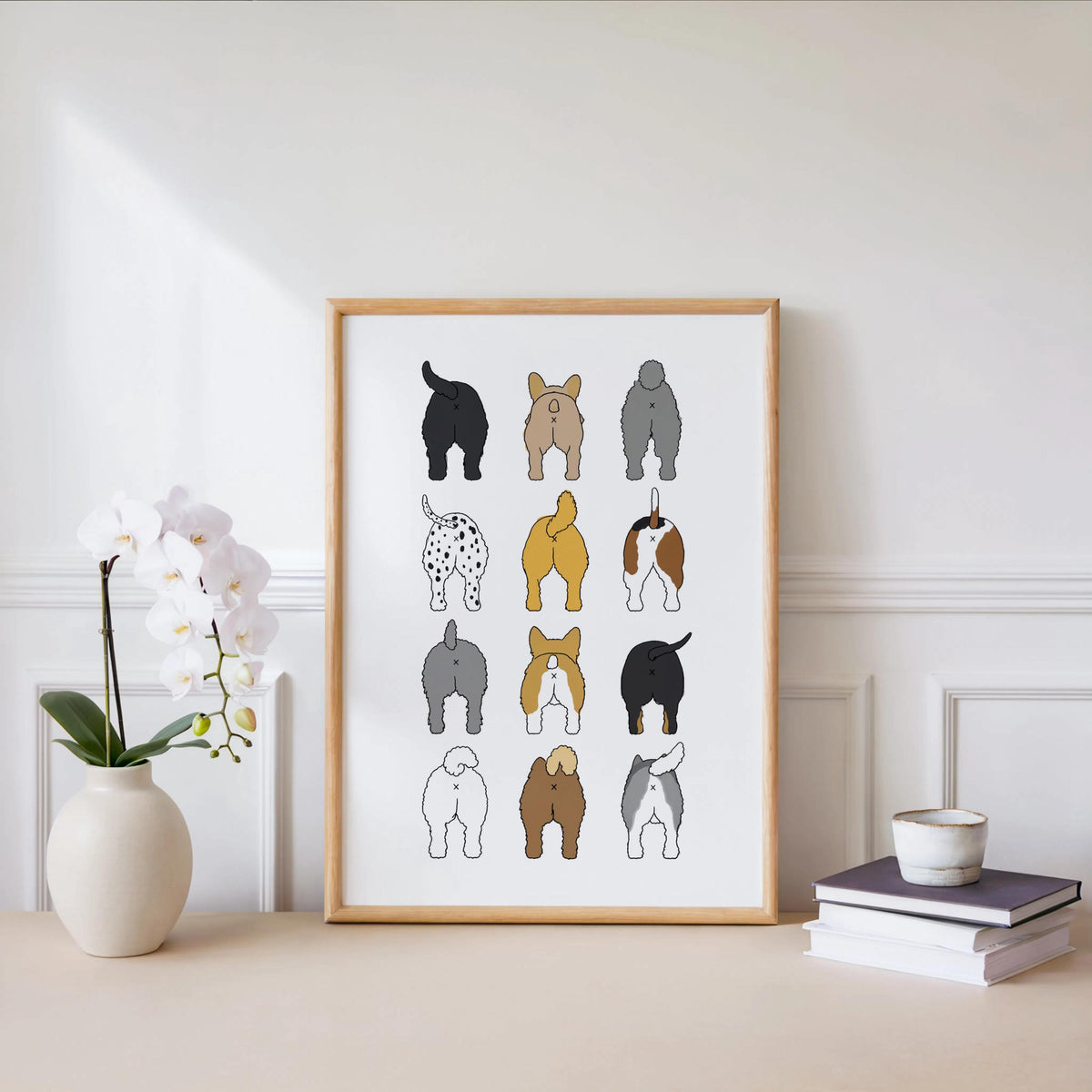 Framed print on a low white shelf next to an orchid and cup, neutral styling, bathroom humor print that doubles as decor