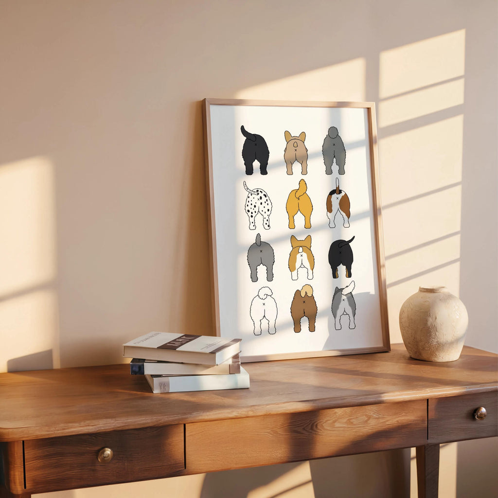 Sunlit wooden console holds propped framed print with books and clay pot, playful dog butts wall art for bathroom