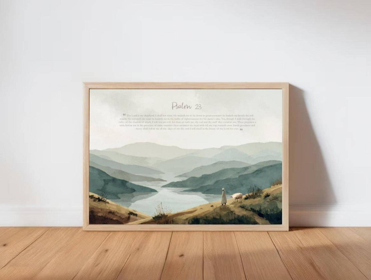 Framed Psalm 23 wall art print leaning on wood floor, layered sage-blue mountains and lone sheep