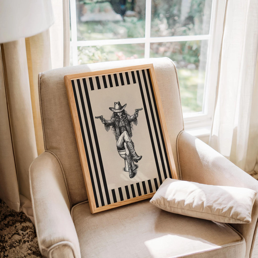 Cowgirl on toilet print placed on cozy armchair by window, natural light, vintage western wall decor