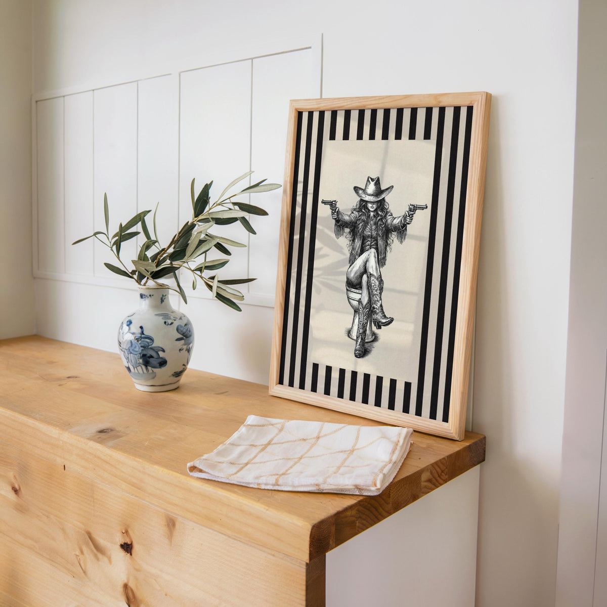 Cowgirl on toilet print propped on wooden console, blue vase styling, funny cowgirl bathroom wall art