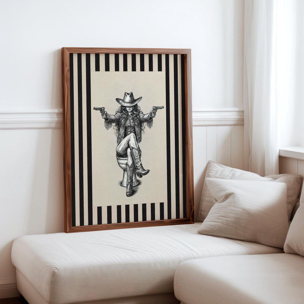 Tall framed cowgirl on toilet print tucked behind sofa cushions, warm neutral tones, rustic farmhouse bathroom art