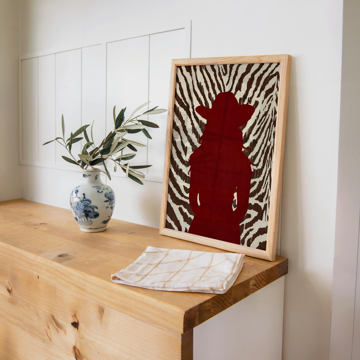 Framed cowgirl silhouette print resting on wooden console beside ceramic vase, animal print western decor vibe