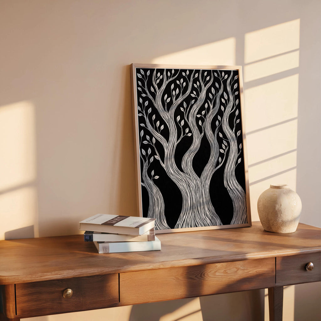 Natural wood-framed black and white forest wall art leaning on rustic desk, woodcut forest print with warm shadows