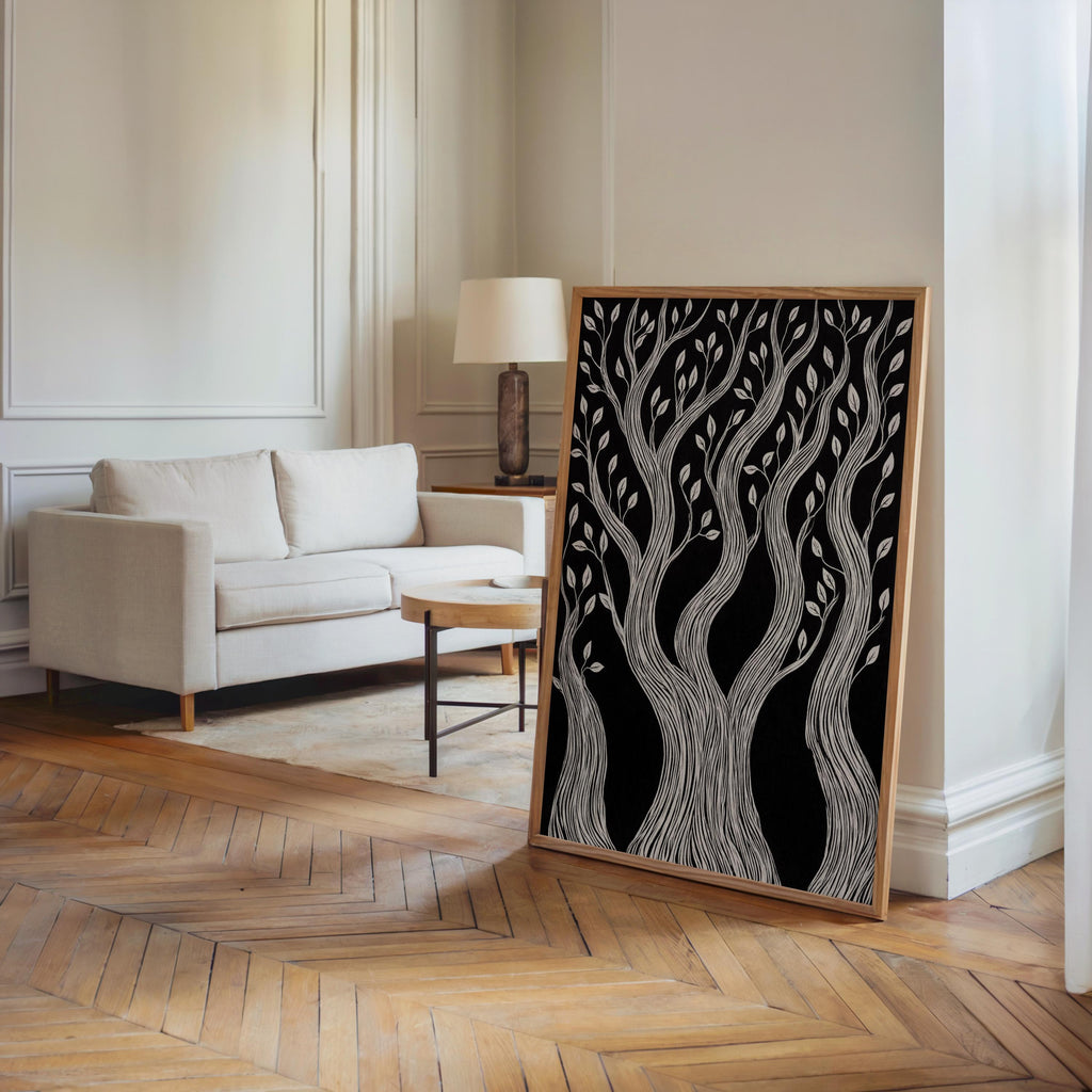 Floor-standing framed monochrome woodland print leaning near sofa in airy room, modern rustic wall art statement