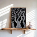 Black and white forest wall art in a natural wood frame, leaning on sunlit shelf with vase, linocut tree print