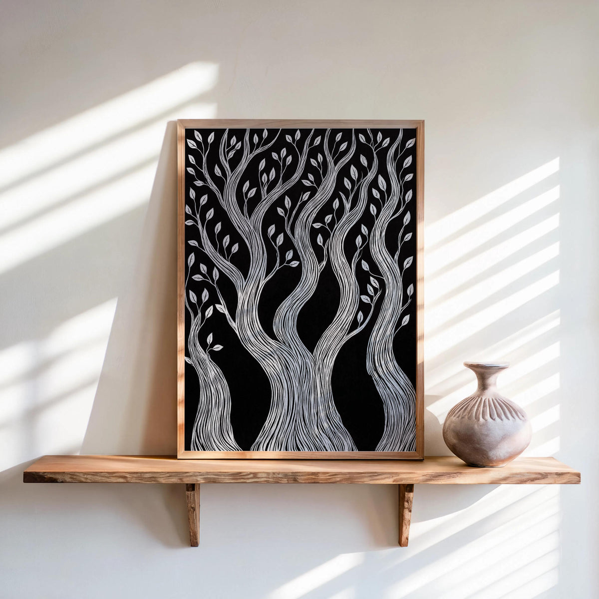 Black and white forest wall art in a natural wood frame, leaning on sunlit shelf with vase, linocut tree print