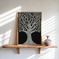 Framed Tree of Life wall art on a floating wood shelf, cream linocut tree on black, vase beside it.