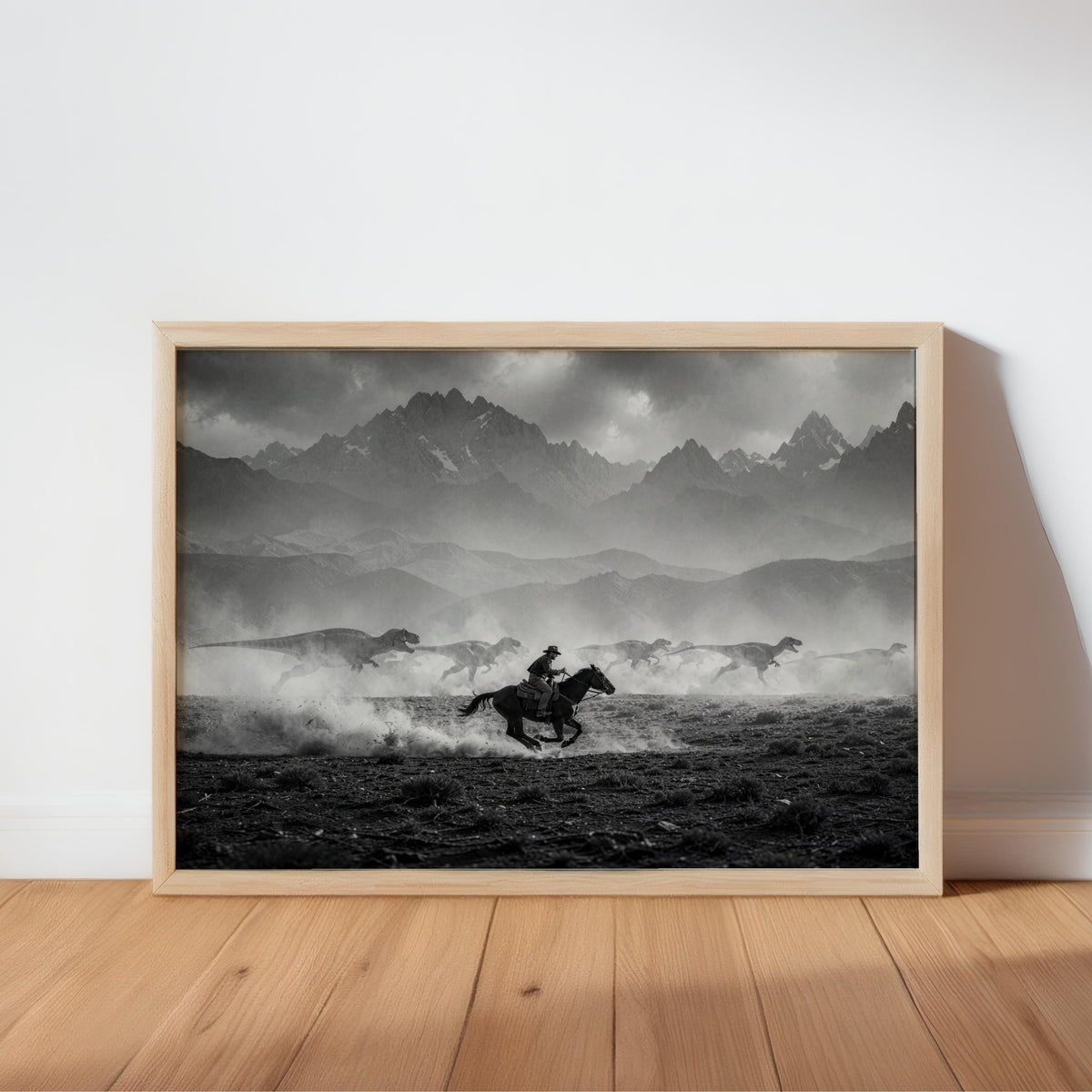 Framed black and white cowboy dinosaur wall art leaning on light hardwood, rugged mountain scene