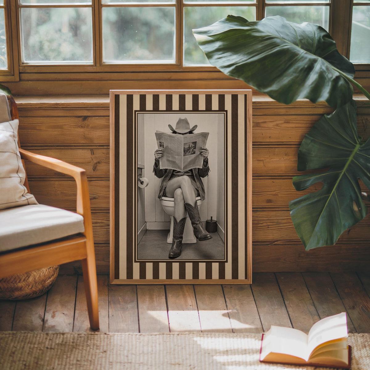 Framed vintage cowgirl print leaning by a wooden chair and large plant, funny cowgirl bathroom art, western bathroom wall decor