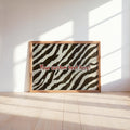 Framed personalized zebra print wall art leaning on a sunlit wooden shelf, bold red typography visible