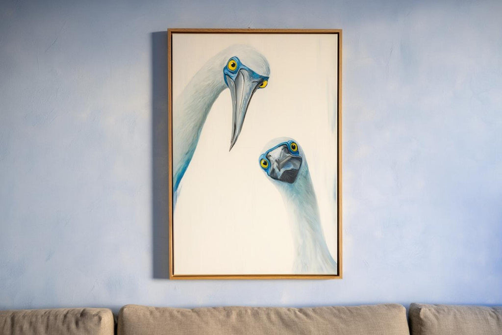Tall framed print hung above sofa area on cool blue-gray wall, coastal bathroom wall art potential, blue footed booby wall art print