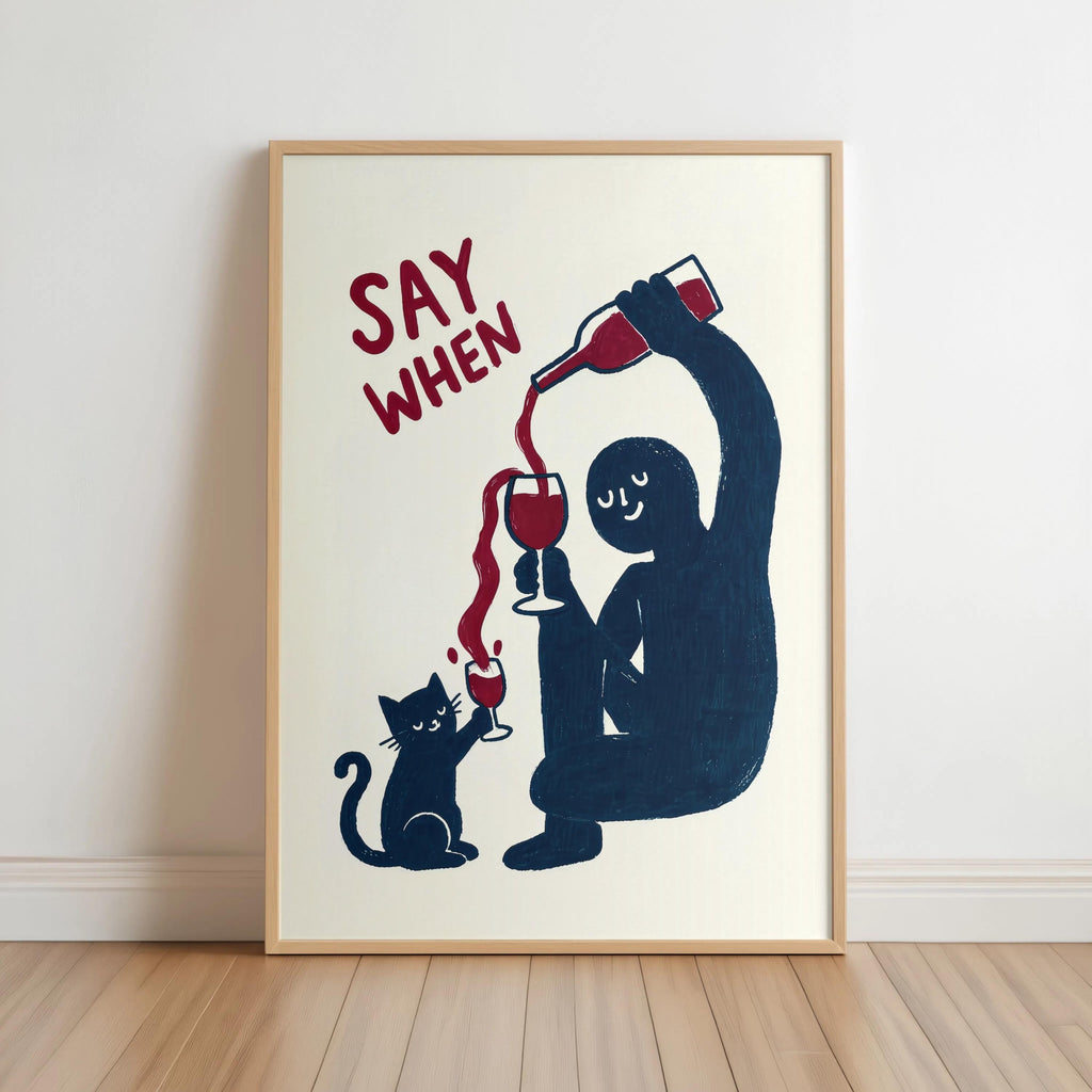 Framed navy SAY WHEN print leaning on warm wood floor, cream backdrop, funny cat wine wall art