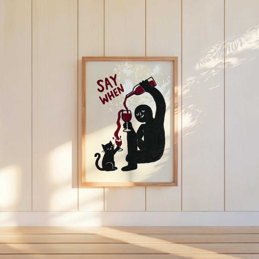 Wall-mounted navy SAY WHEN poster on white paneled wall, sunlit shadows, quirky dining room decor, funny cat wine wall art