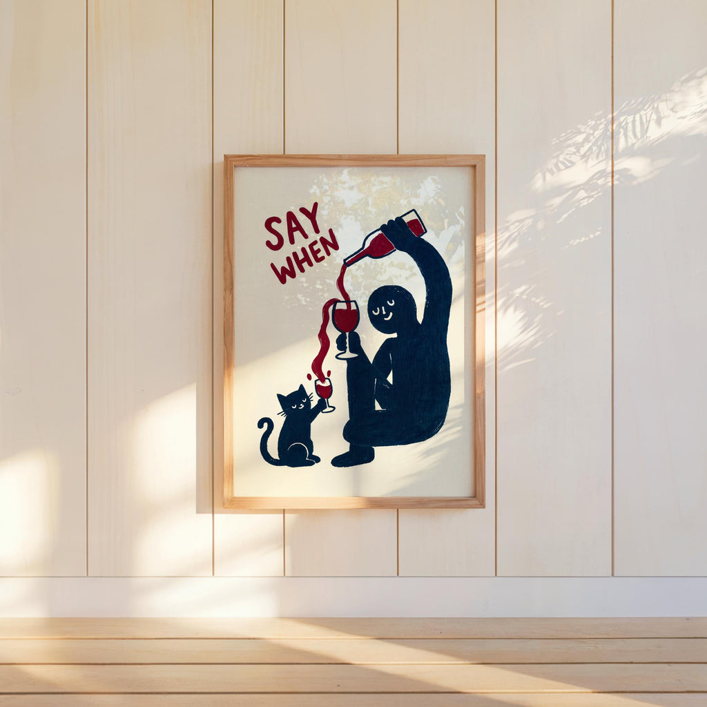 Framed navy SAY WHEN poster on paneled wall, angled sunlight and warm tones, home bar wall art, funny cat wine wall art