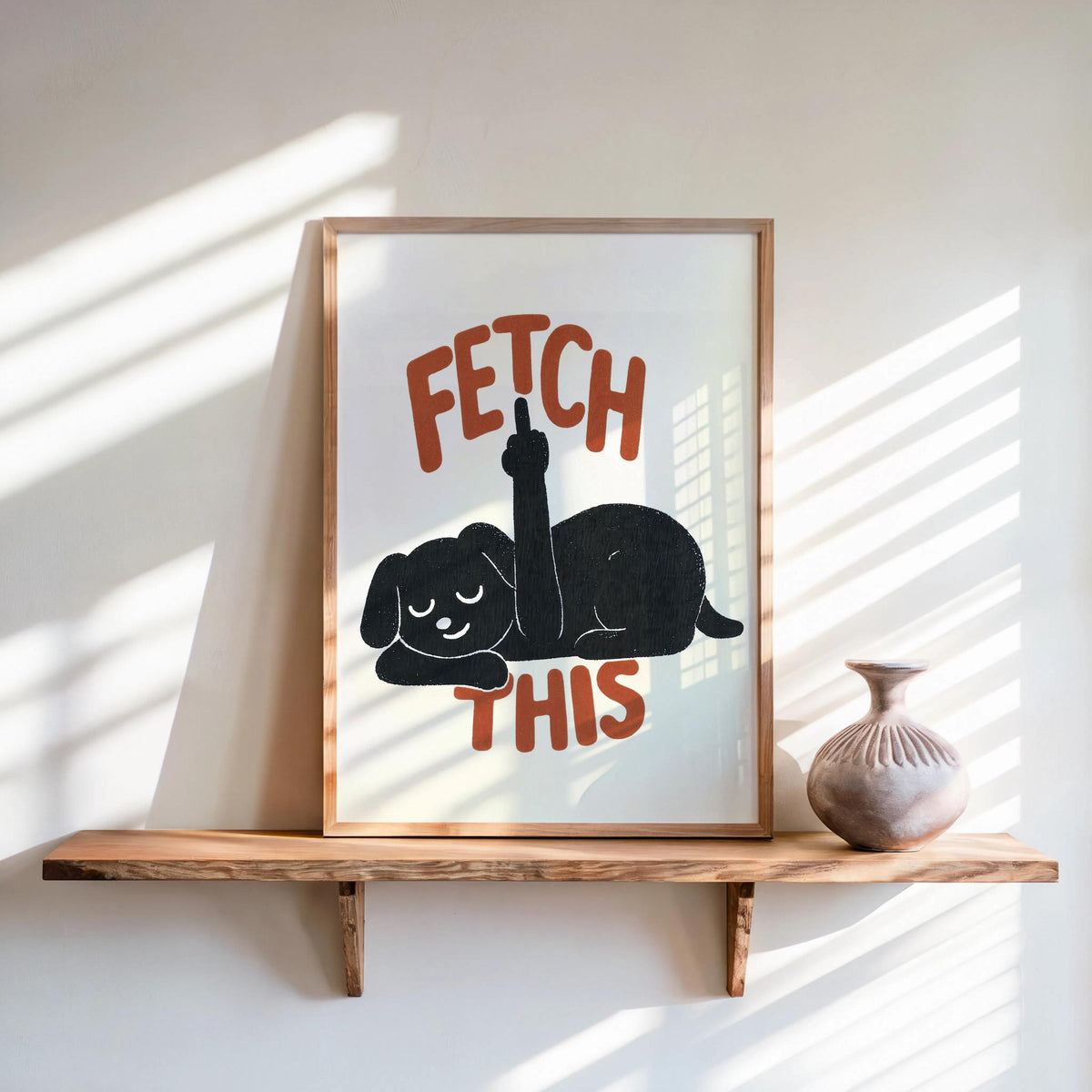 Sunlit shelf scene with framed cream poster, charcoal dog and burnt orange lettering, cheeky dog print for dog lover gift