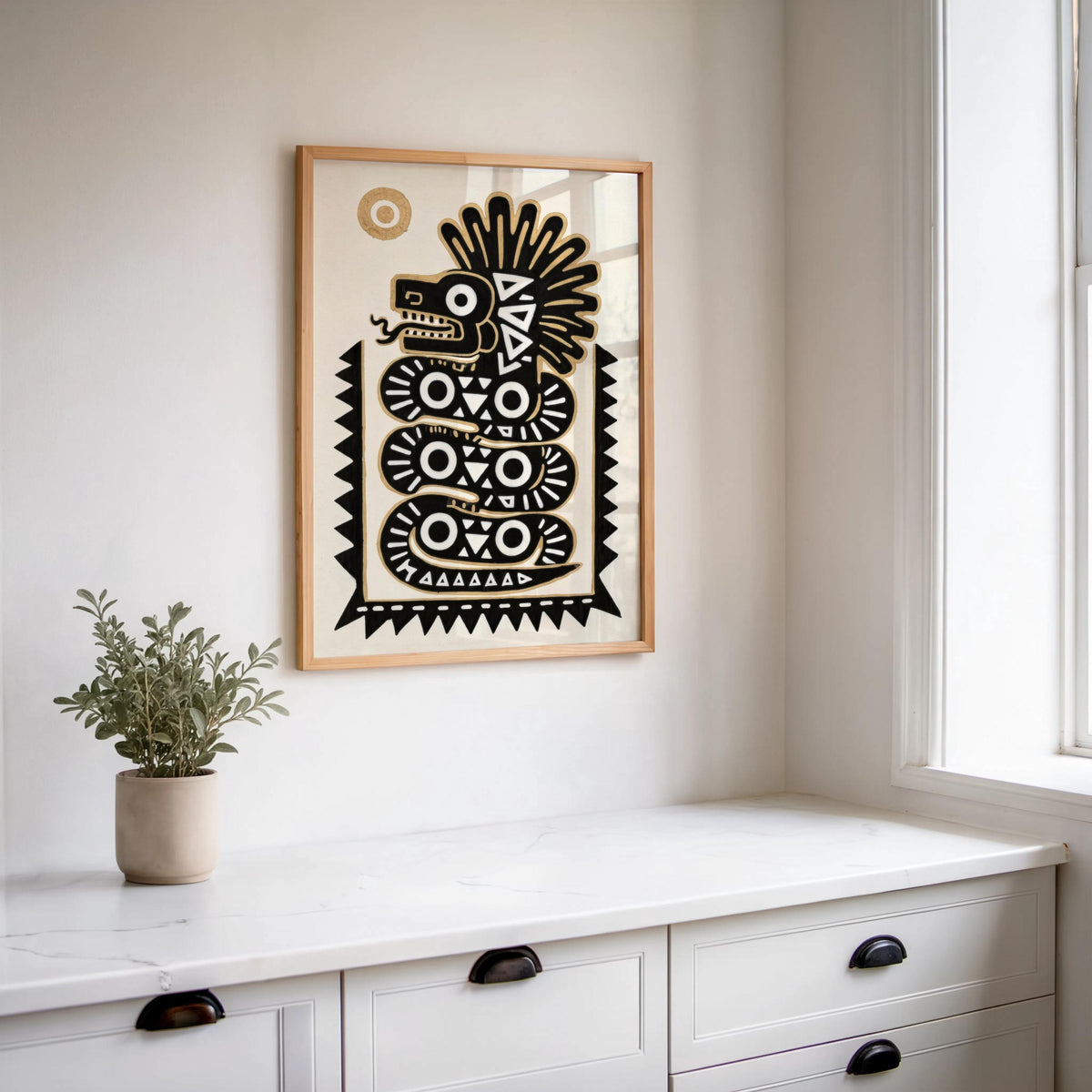 Centered quetzalcoatl art print above white cabinetry and potted plants, crisp black and gold graphic contrasts