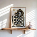 Leaning light-wood framed quetzalcoatl art print on a floating shelf, sunlit boho styling and earthen vase
