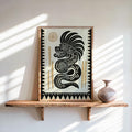 Framed Quetzalcoatl wall art leaning on a wood shelf, bold black-and-cream serpent with gold sun.