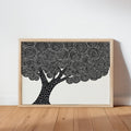 Framed black and white tree wall art leaning on a wooden table, bold linocut canopy detail