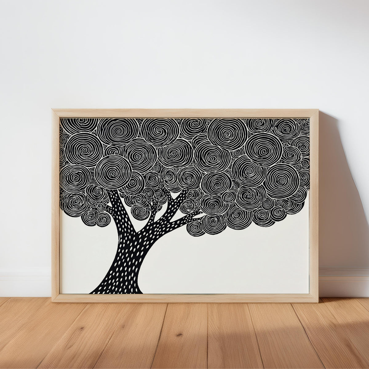 Framed black and white tree wall art leaning on a wooden table, bold linocut canopy detail