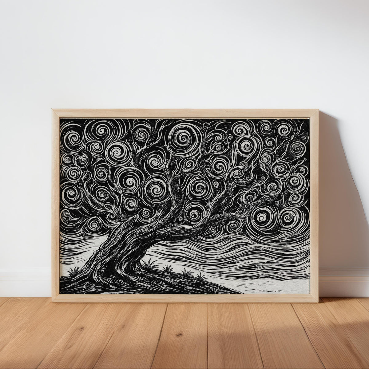 Horizontal black and white tree linocut print in a natural wood frame, leaning on hardwood floor, bold white carved lines