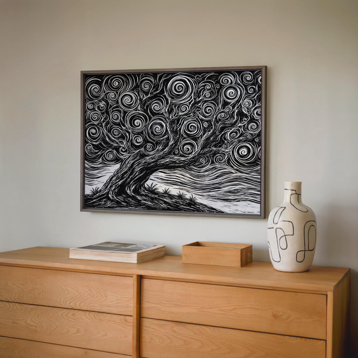 Black and white tree linocut print centered above an oak dresser with ceramics, gnarled tree poster echoing vintage woodblock aesthetics