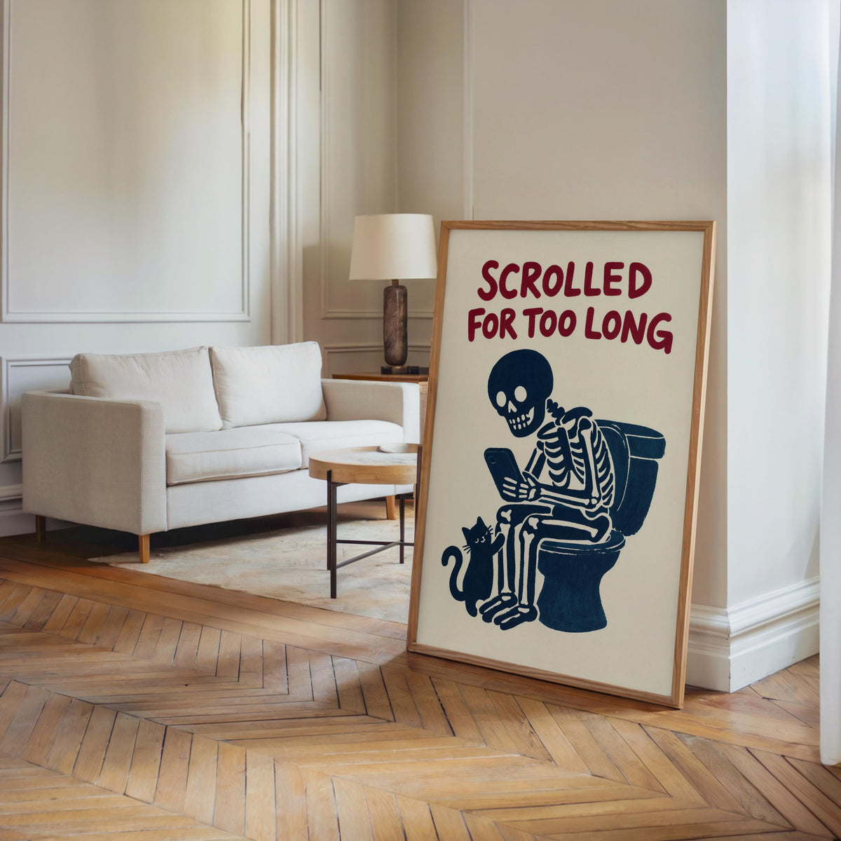 Leaning framed print beside living room sofa, quirky goth print vibe, navy skeleton and cat on cream paper