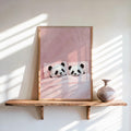 Blush pink sleeping panda wall art, framed on a wooden shelf with a vase, sunlit striped shadows, cuddling panda print