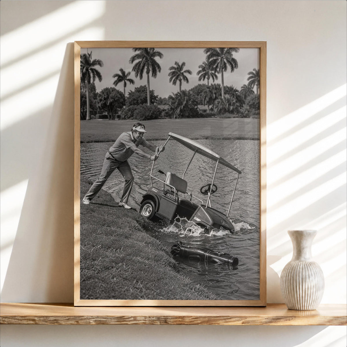 Angry golfer poster in wood-frame mockup, black and white, palm-lined lake on shelf.