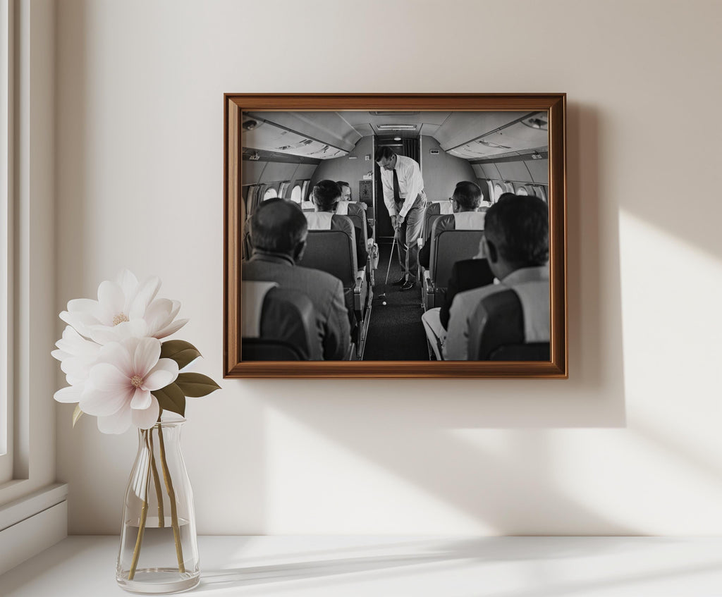 Brown frame above a small table with vase, monochrome golfer swinging in an airplane cabin, vintage golf print for wall decor