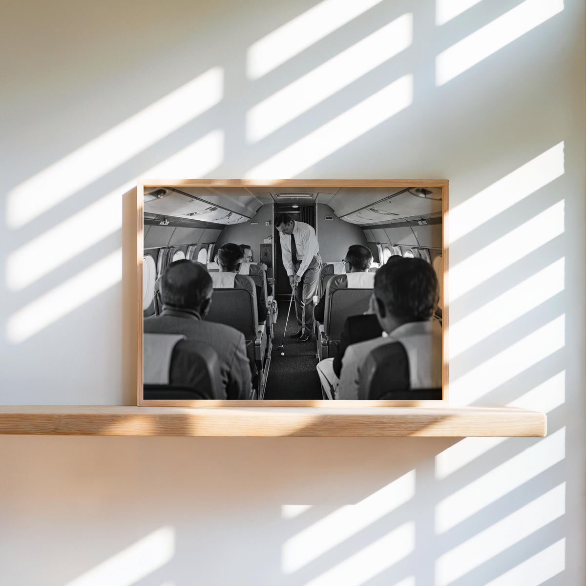 Wood frame on sunlit ledge, surreal black and white golf art of a mid swing inside an aircraft aisle