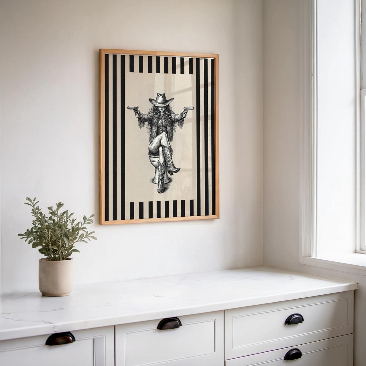 Vertical framed cowgirl on toilet print hung above white counter, succulent styling, funny cowgirl bathroom wall art