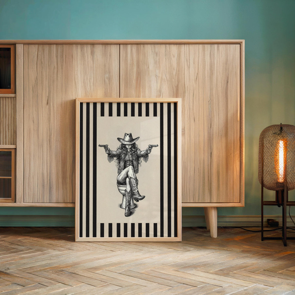 Large framed funny cowgirl bathroom wall art leaning against teal wall, rustic frame, southwestern vibe
