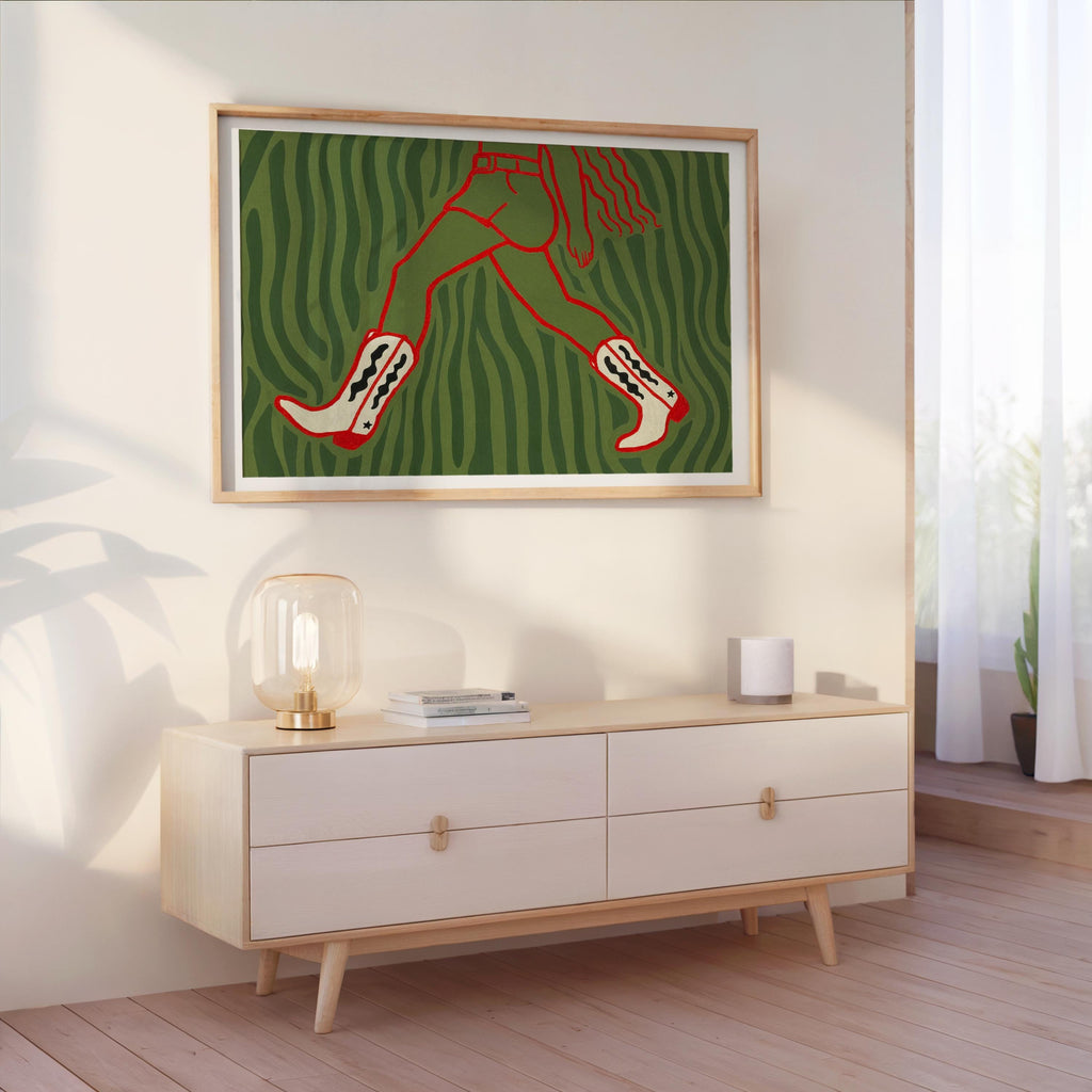 Green cowgirl wall art print framed on wall above console, playful western fashion print with bold red boots motif