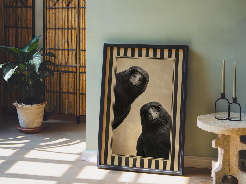 Two crow art print leaning on a sunlit floor beside a potted plant and pottery, vintage crow wall art style