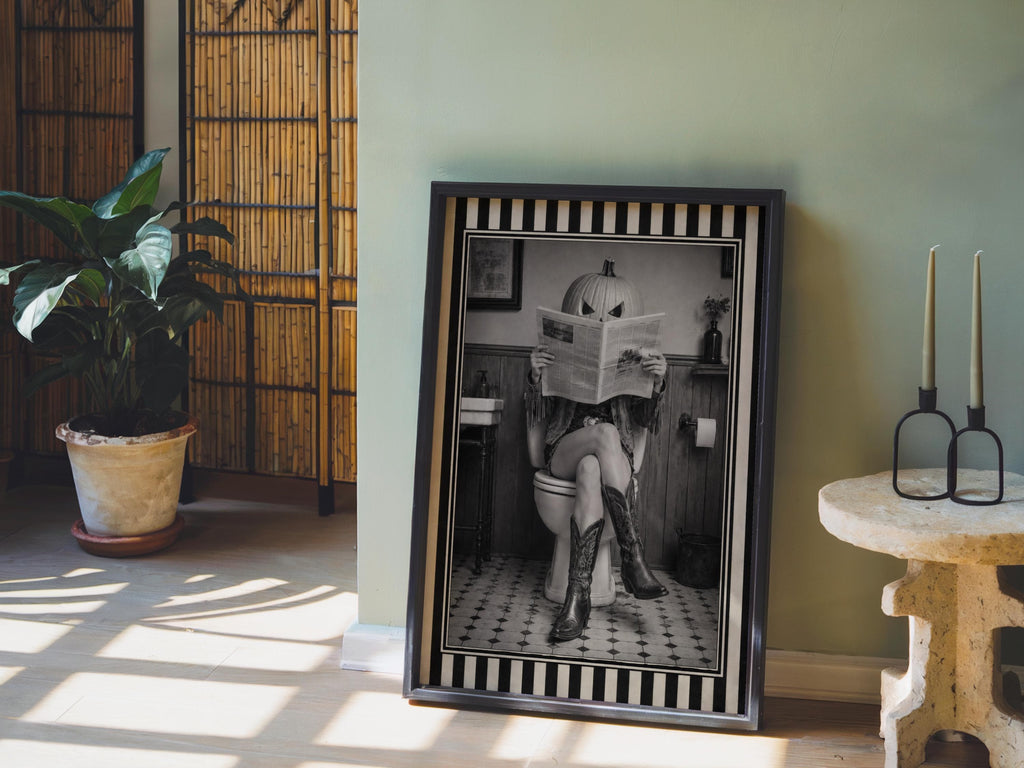Monochrome pumpkin head cowgirl art print leaning near candles and plant, quirky Western bathroom art vibe