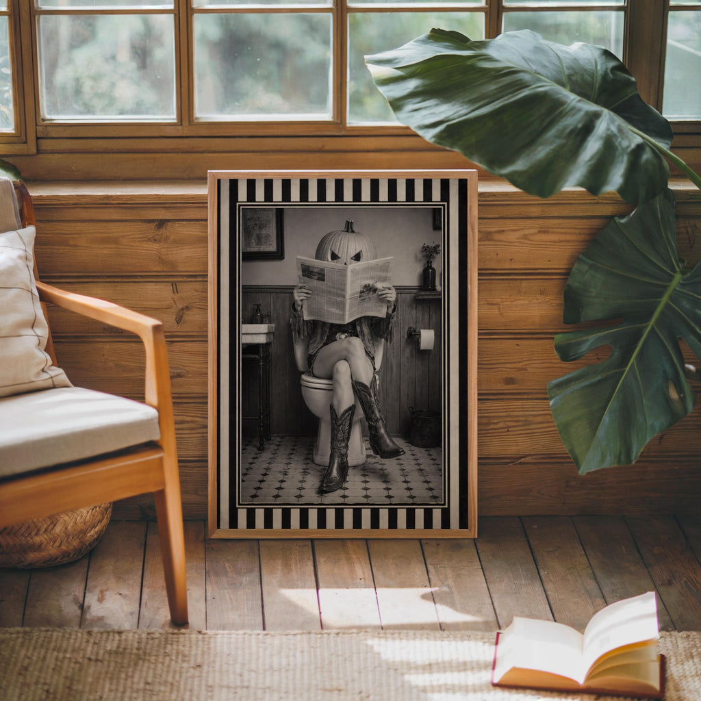 Monochrome pumpkin head cowgirl art print resting next to chair and large leaf, weird bathroom art mood